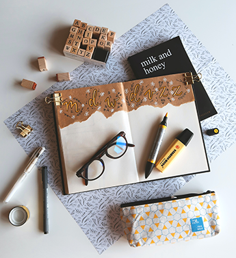 Desk blotter with planner book, writing utensils, paper clips, eyeglasses, and alphabet stamps